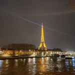 Eiffel Tower lit up at night with its spotlight shining across the Paris sky